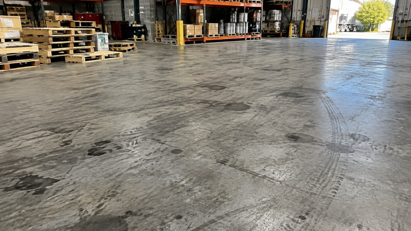 Walk-behind floor scrubber removing oil stains from a concrete factory floor.png
